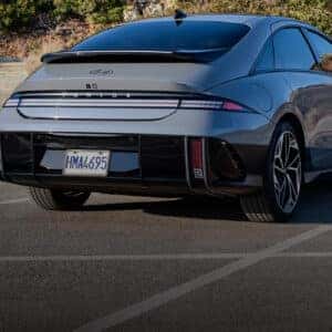 Rear view of a Hyundai IONIQ 6 parked in an open lot, showcasing its aerodynamic design and pixel-style LED taillights.