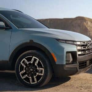 the front passenger side profile of a blue santa cruiz parked next to an ocean overlook with a rock face in the background
