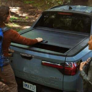 a woman and a man in the woods next to a blue santa cruz about to go hiking with packs on their back.