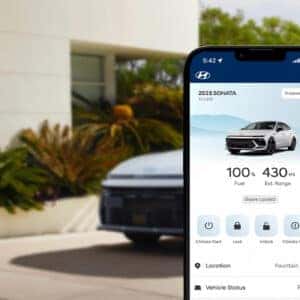 A smartphone displaying the Hyundai Bluelink app interface for the 2025 Hyundai Sonata N Line, with a white Sonata parked in the background in front of a modern house.