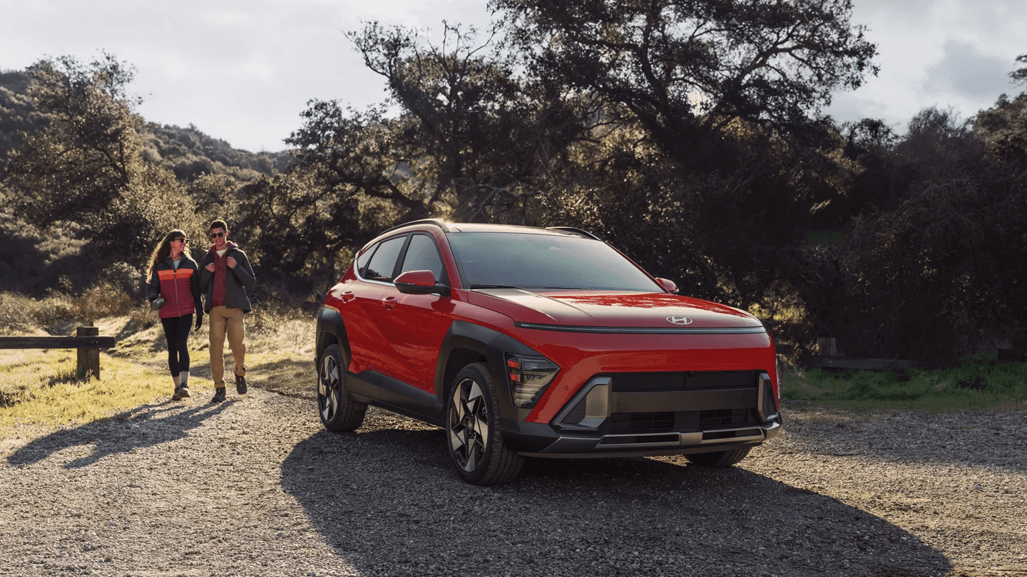 A man and woman walking towards a red car.