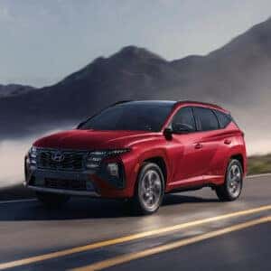 side profile of a red tucson hybrid driving on a mountain road with fog in the distance.