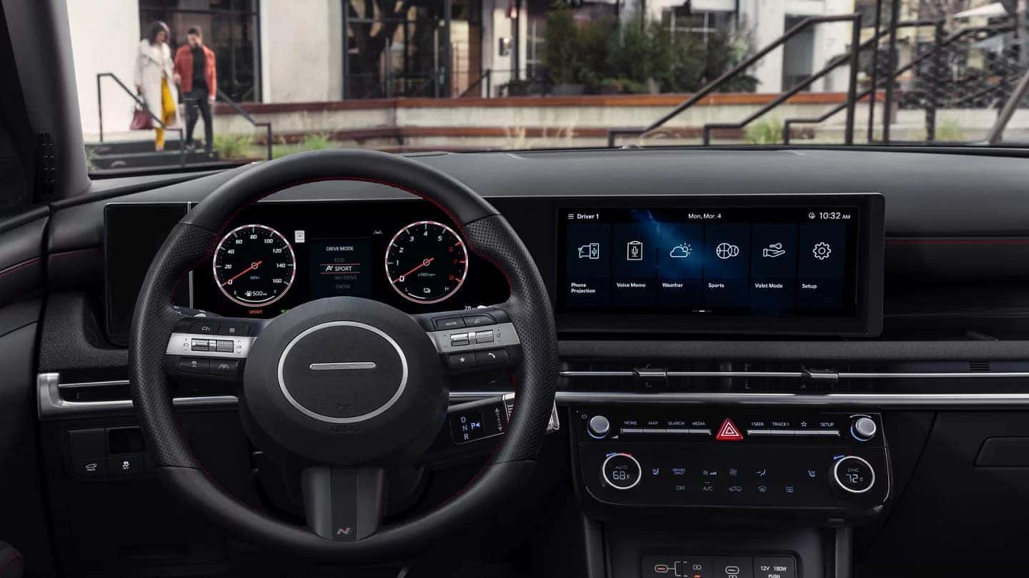 Driver's perspective interior shot of the 2025 Hyundai Tucson showing the panoramic digital displays, steering wheel, and minimalist center console against a mountain backdrop.