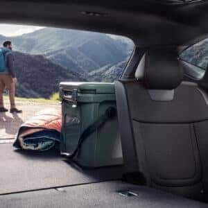 Rear cargo area of the 2025 Hyundai Tucson with the tailgate open, showing a cooler and blanket packed for an adventure, with two hikers visible outside against mountains.