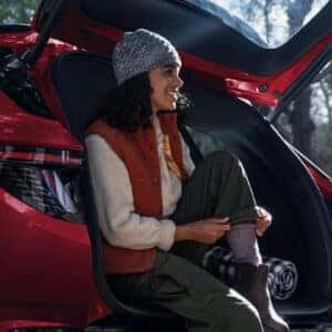 Woman sitting in the open tailgate of a red 2025 Hyundai Tucson, adjusting her hiking boots with a forest setting in the background.