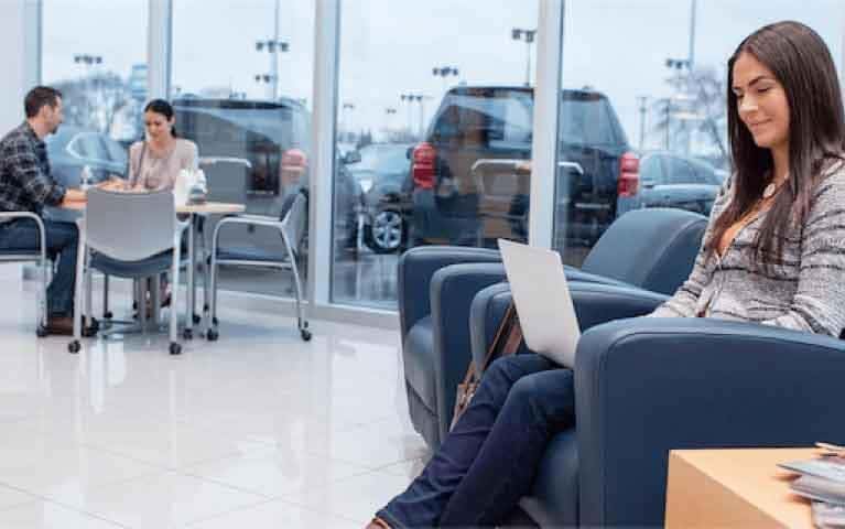 A girl sitting inside a dealership, looking at her computer.
