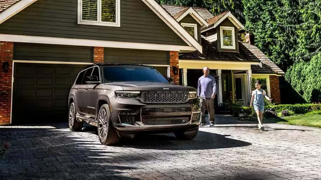 Parent and child walking towards 2025 Grand Cherokee parked in driveway of home