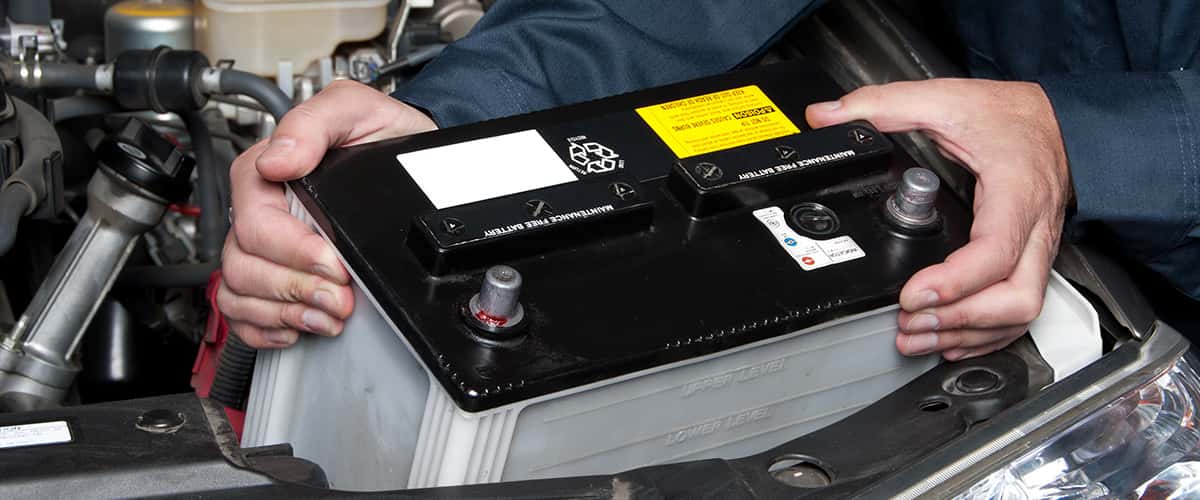 mechanic putting mazda car battery into engine area 