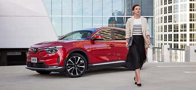 A woman walking away from a red VinFast VF 8